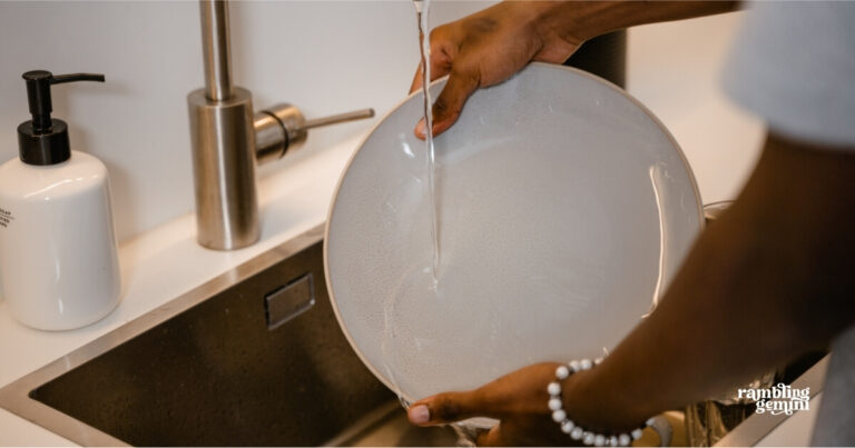 Bright kitchen sink with a person rinsing a plate under running water.
